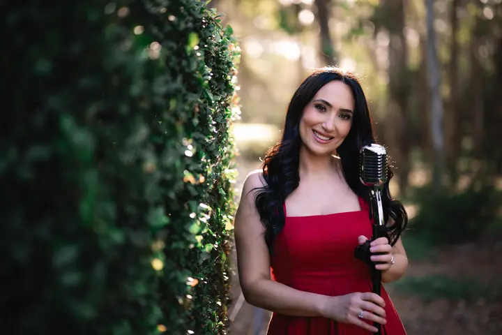 Linda Dagher holding a vintage microphone in a garden setting